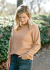 Blonde model wearing a camel color turtleneck sweater.