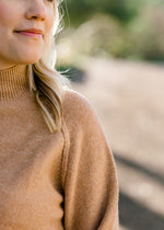 Close up view of raw hemline on Blonde model wearing a camel color sweater.