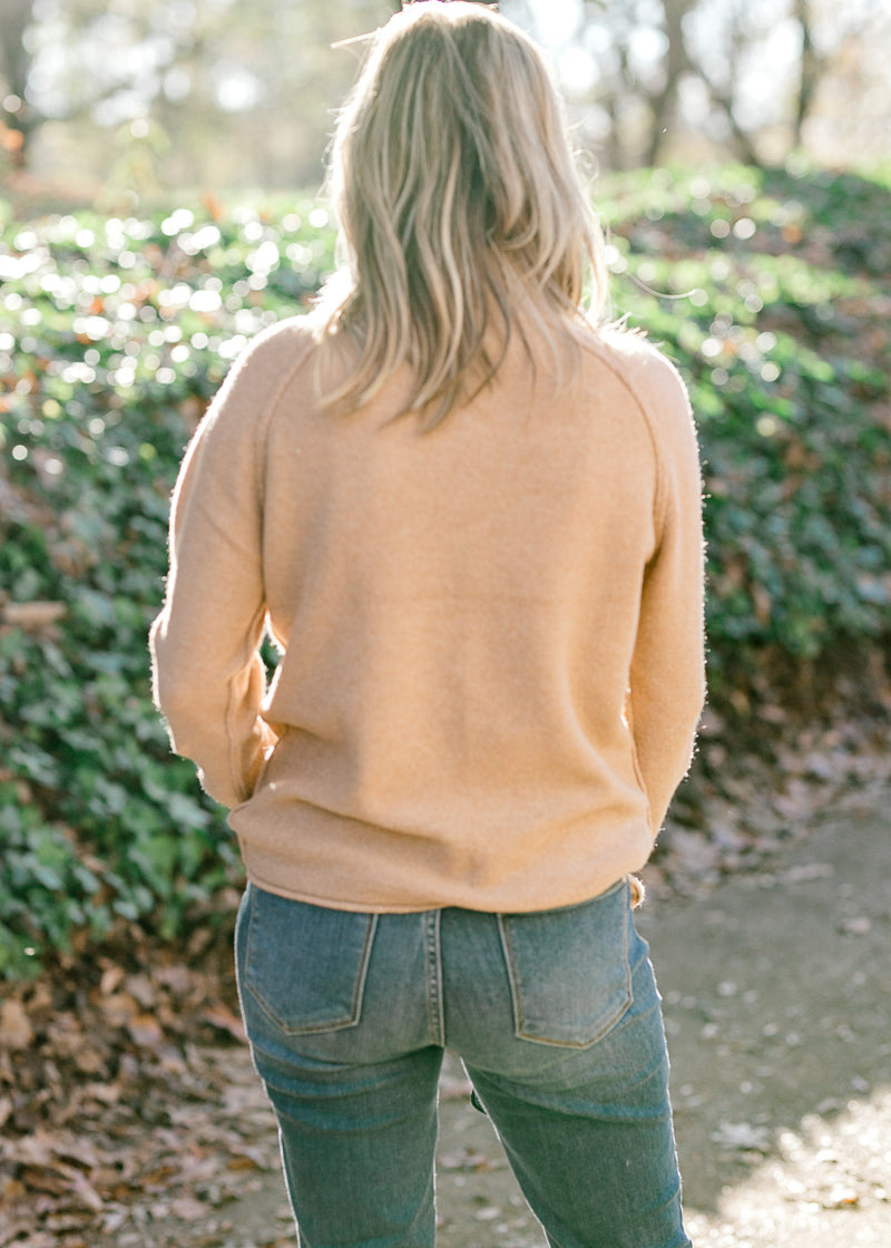 Back view of Blonde model wearing a camel color turtleneck sweater.