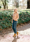 Blonde model wearing a camel color turtleneck sweater with jeans and heeled mules.