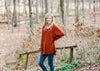 Blonde model wearing deep rust long sleeve top and jeans.