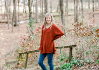 Blonde model wearing deep rust long sleeve top and jeans.