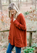 Side view of Blonde model wearing deep rust long sleeve top.