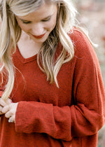 Close up detail of Blonde model wearing deep rust long sleeve top.