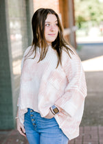 Brunette model wearing pink and white sweater with jeans.