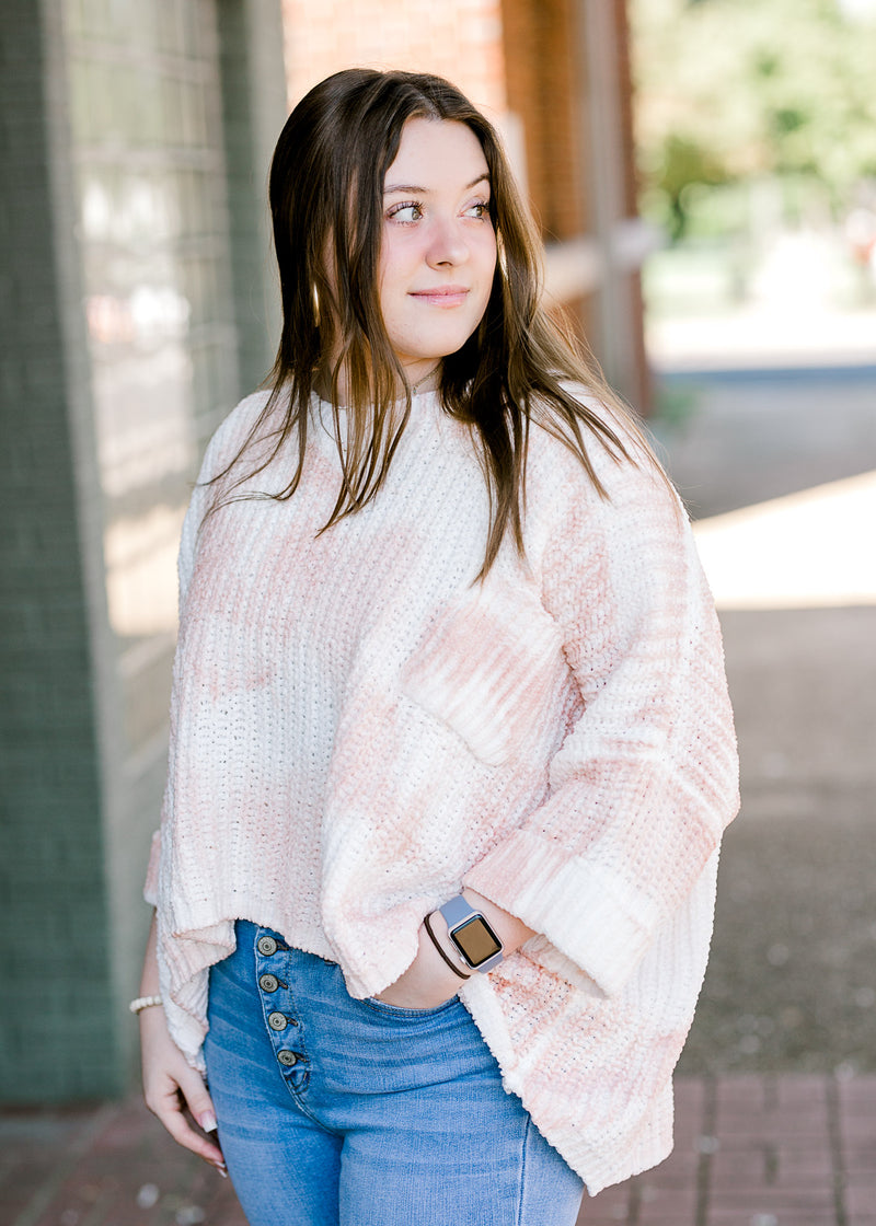 Brunette model wearing pink and white sweater with jeans.