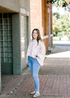 Brunette model wearing pink and white sweater with jeans and sandals.
