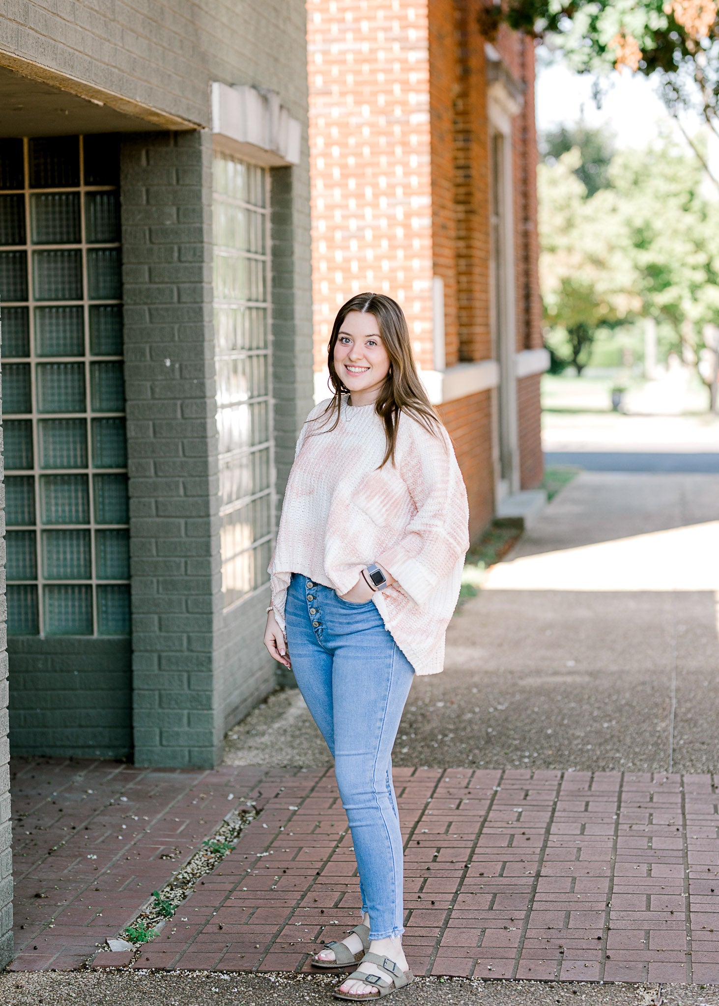 Brunette model wearing pink and white sweater with jeans and sandals.