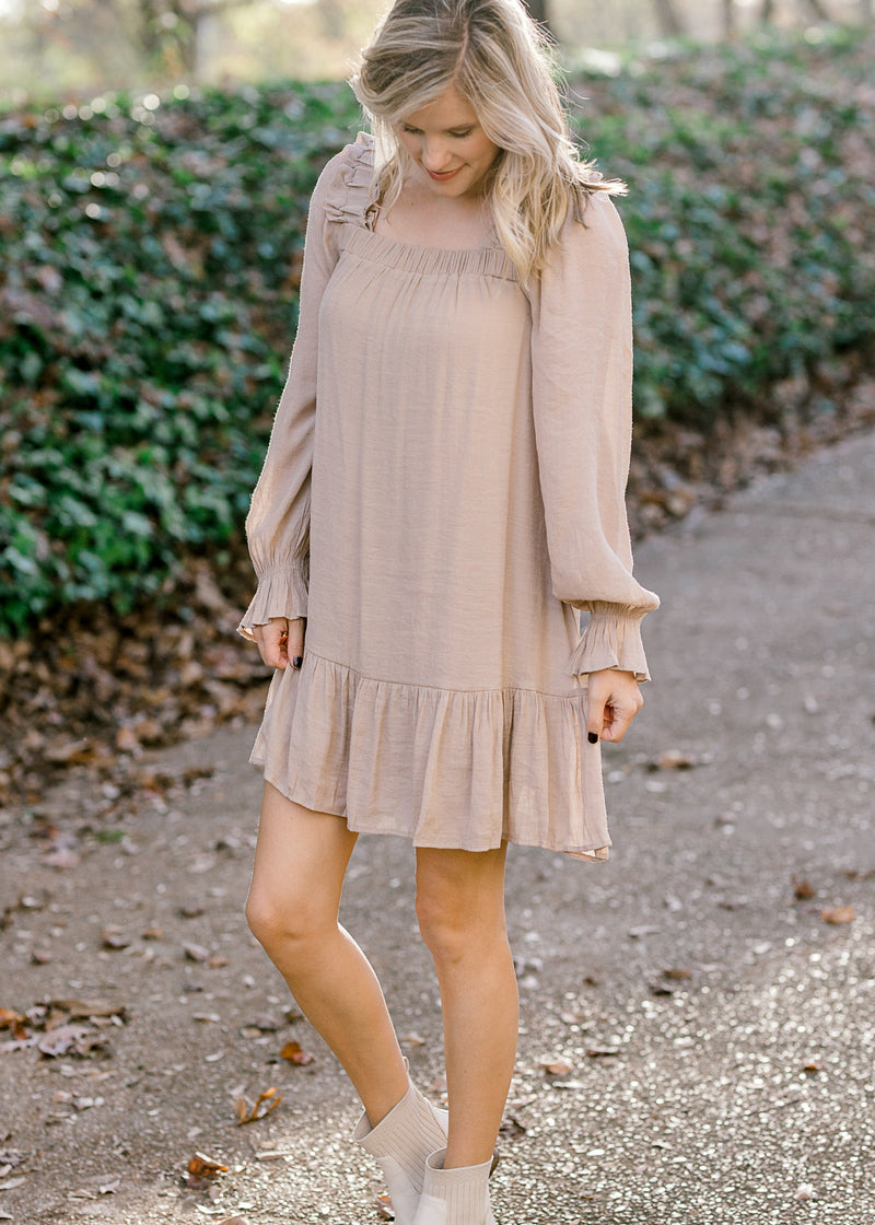 Blonde model wearing sand colored, above the knee dress. 