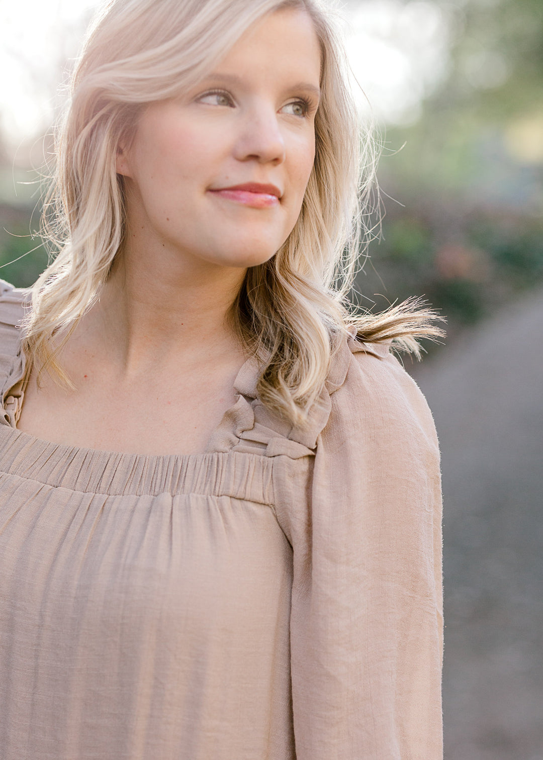 Close up view of Blonde model wearing sand colored dress with square neckline. 