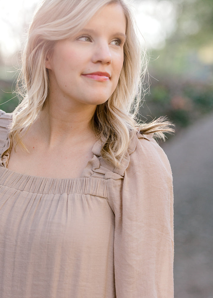 Close up view of Blonde model wearing sand colored dress with square neckline. 