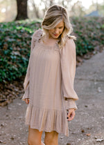 Blonde model wearing sand colored, above the knee dress, with ruffle at bottom. 
