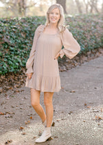 Blonde model wearing sand colored, above the knee dress with booties. 