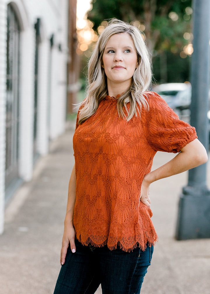 Blonde model wearing rust top with lace overlay.