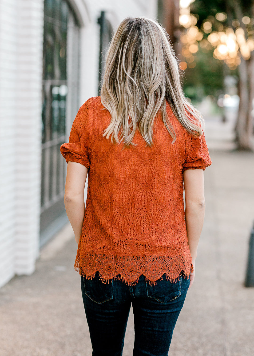 Back view of Blonde model wearing rust top with lace overlay.
