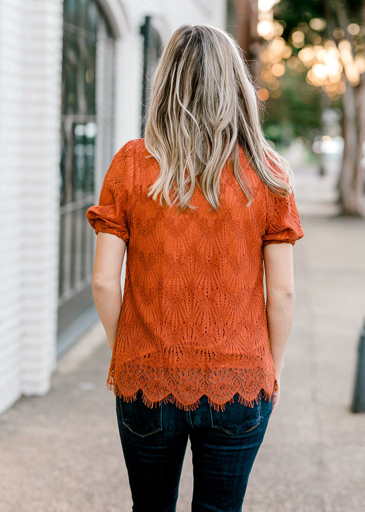 Back view of Blonde model wearing rust top with lace overlay.