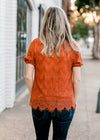 Back view of Blonde model wearing rust top with lace overlay.