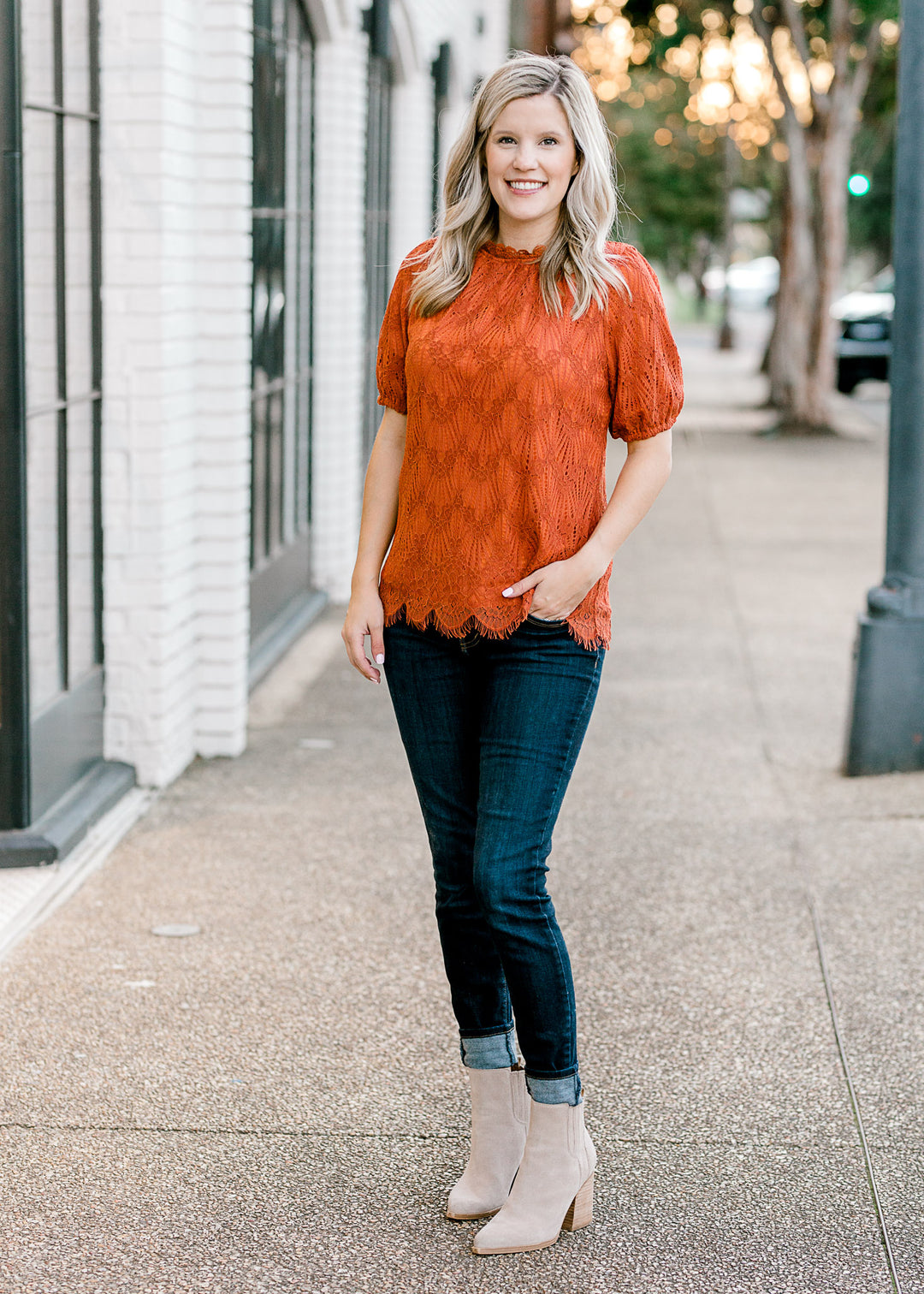 Blonde model wearing jeans and booties with a rust top with lace overlay. 