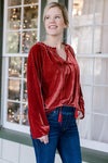 Blonde model wearing red velvet top with drawstring neck and jeans.