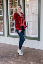 Blonde model wearing red velvet top with drawstring neck, jeans and booties.