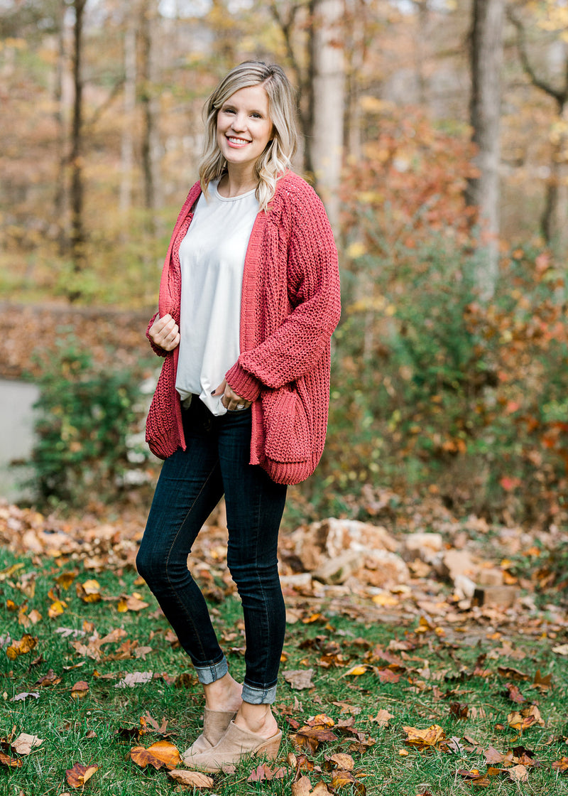 Blonde model wearing a rust cable knit cardigan with a white top, jeans and mules. 