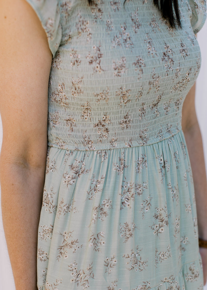 Close up view of smocked bodice and cream floral detail on a sage midi dress. 