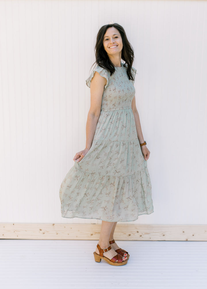 Model wearing a sage tiered midi dress with a smocked bodice and flutter capped sleeves with heels.