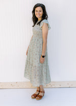 Model wearing a sage midi dress with a floral pattern and a smocked bodice with flutter sleeves.