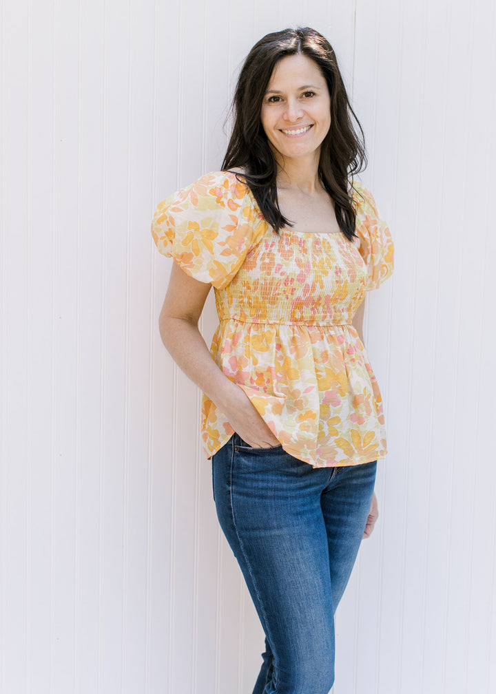 Model wearing a yellow and pink floral babydoll top with a smocked bodice and short bubble sleeves. 