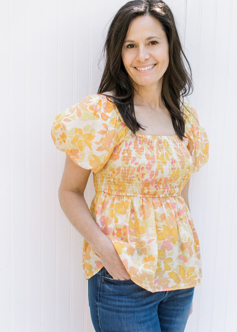 Model wearing a yellow and pink floral babydoll top with square neckline and a smocked bodice. 