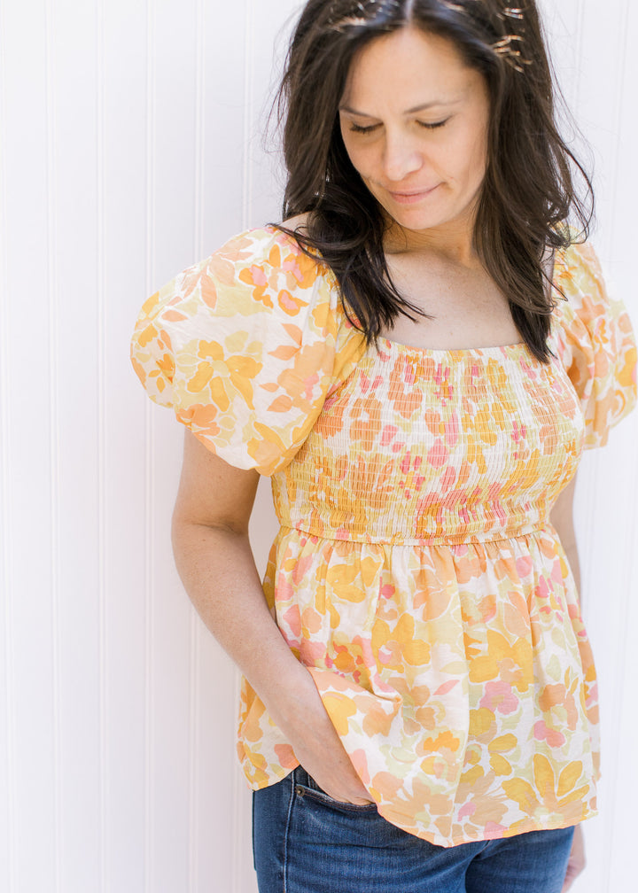 Close up view of smocked bodice and short bubble sleeves on a yellow and pink floral top. 