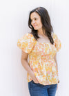 Model wearing a yellow and pink floral babydoll top with a square neckline and a bubble short sleeve