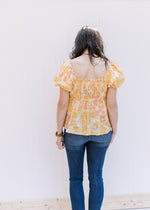 Back view of Model wearing a yellow and pink floral top with a smocked bodice and bubble sleeves. 