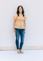 Model wearing jeans and sandals with a yellow and pink floral babydoll top with a smocked bodice. 