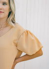 Close up view of bubble short sleeves on a model wearing a tan above the knee dress. 