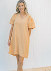 Model wearing a tan, above the knee, V-neck dress with pockets and bubble short sleeves. 