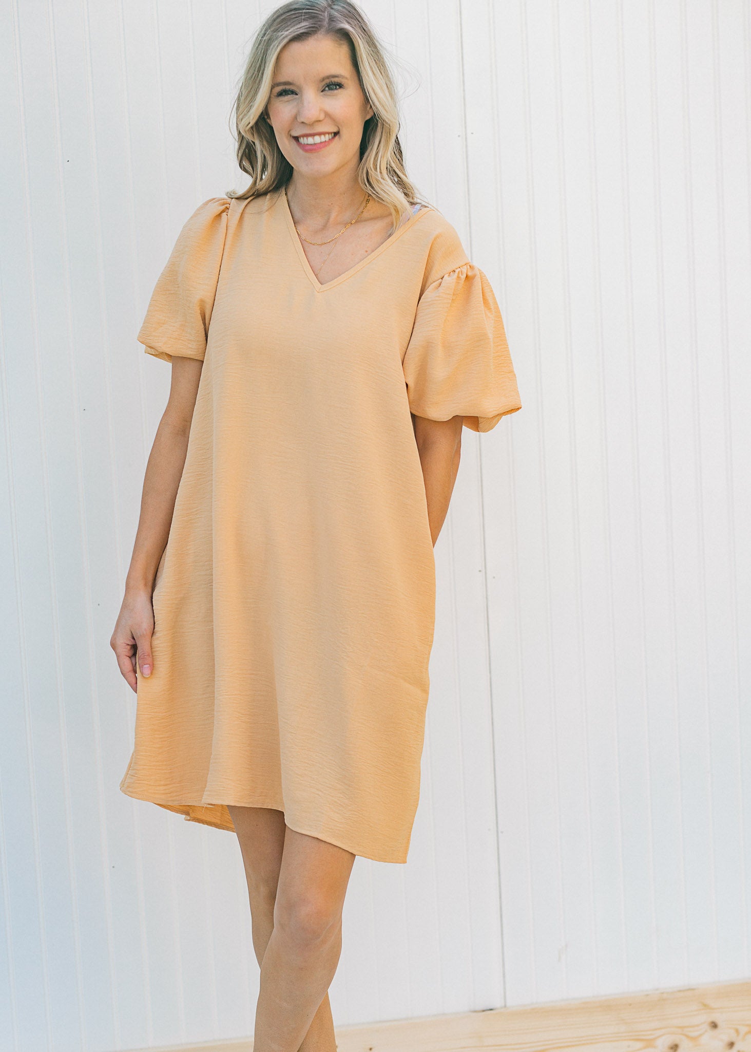 Model wearing a tan, above the knee, V-neck dress with pockets and bubble short sleeves. 