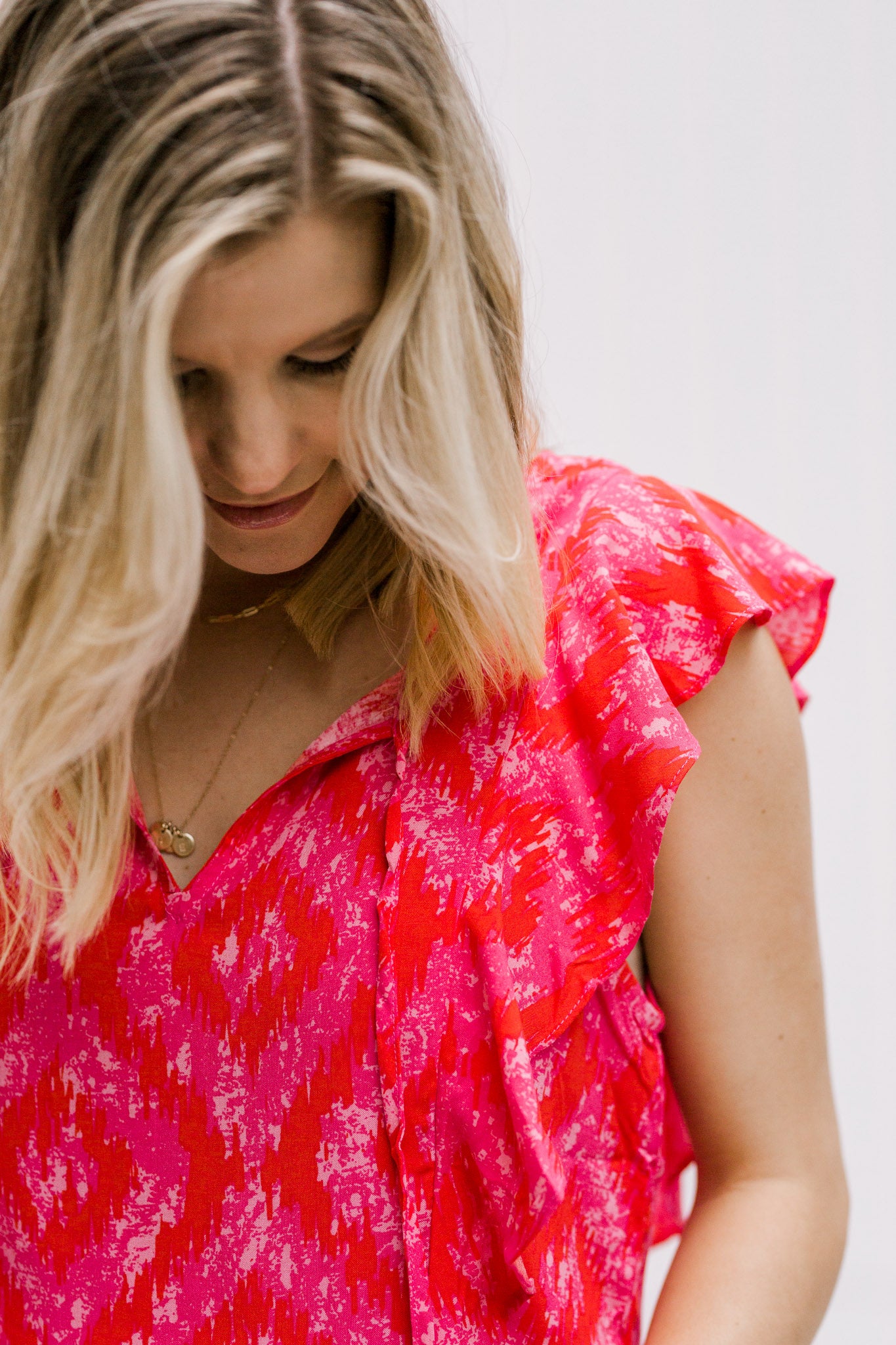 Close up view of Blonde model wearing a bright pink top with capped sleeves.