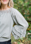 Detail view of lace on square neckline and ruffle on long sleeves.