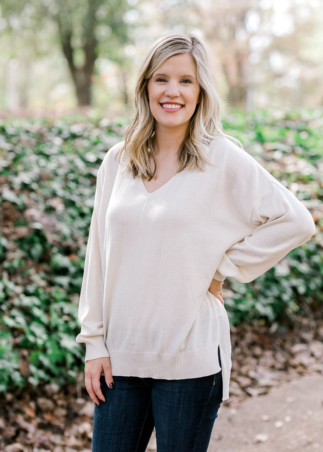 Blonde model wearing cream, v-neck sweater. 