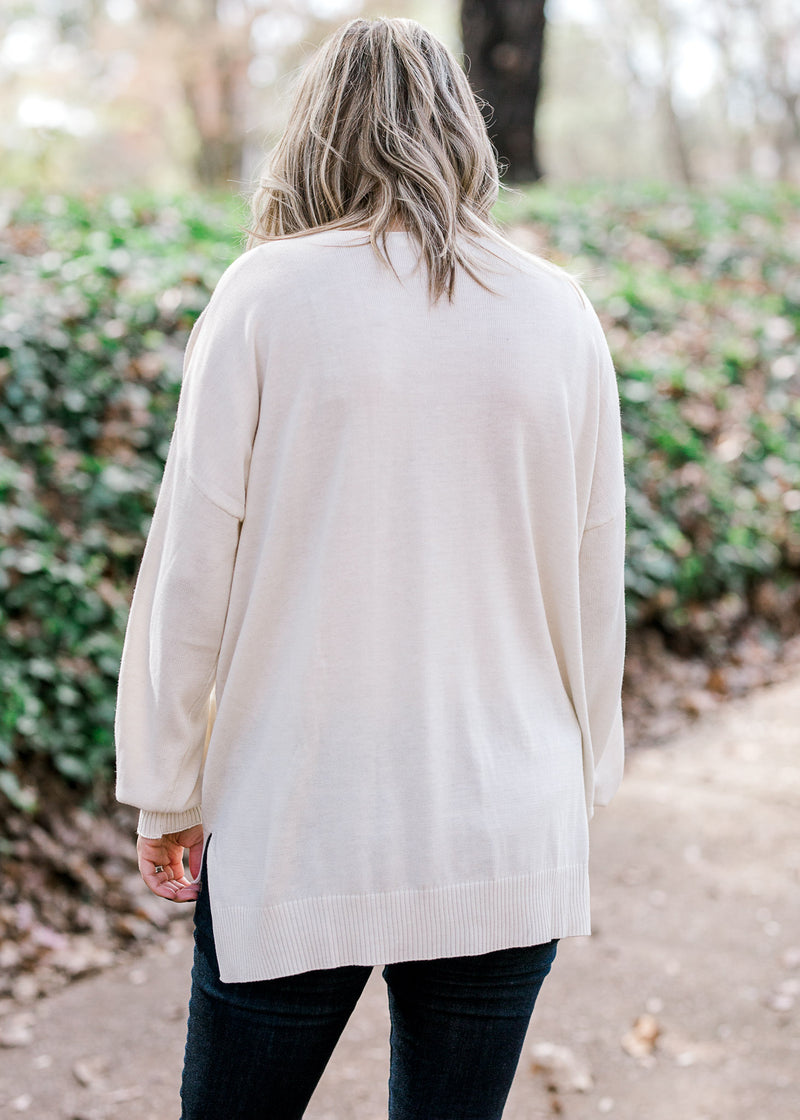 Back view of Blonde model wearing cream, v-neck sweater. 