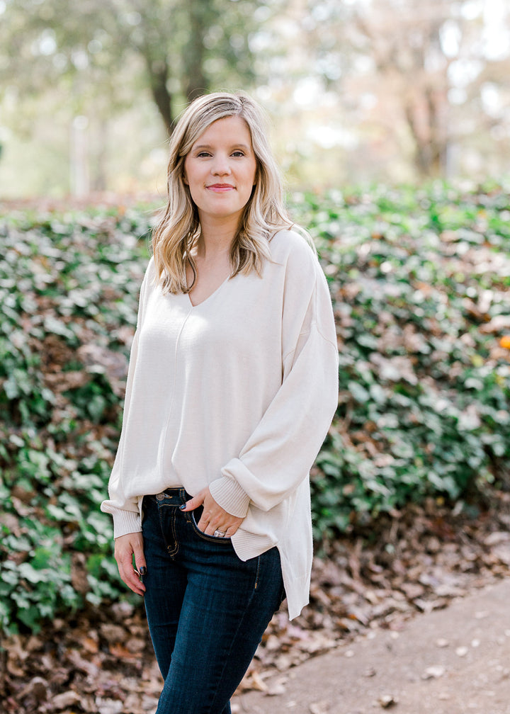 Blonde model wearing cream, v-neck sweater with jeans. 