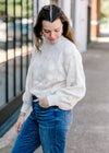 Brunette model wearing cream sweater with shell stitching.