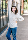 Brunette model wearing cream sweater with jeans.