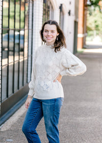 Brunette model wearing cream sweater with jeans.