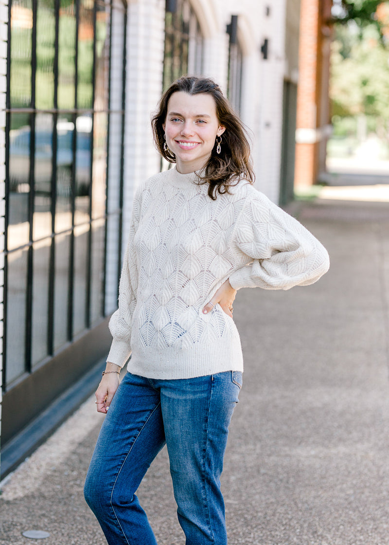 Brunette model wearing cream sweater with jeans.