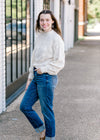 Brunette model wearing cream sweater with jeans and sandals.