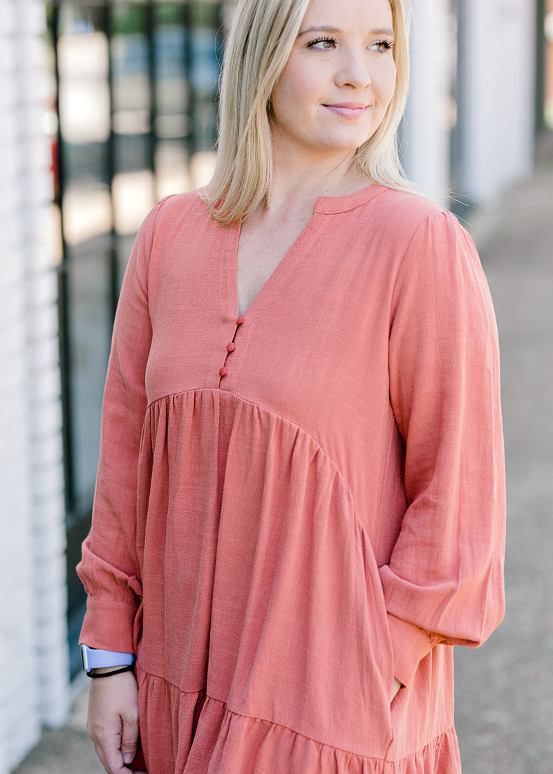 Blonde model wearing burnt coral dress with three detail buttons.
