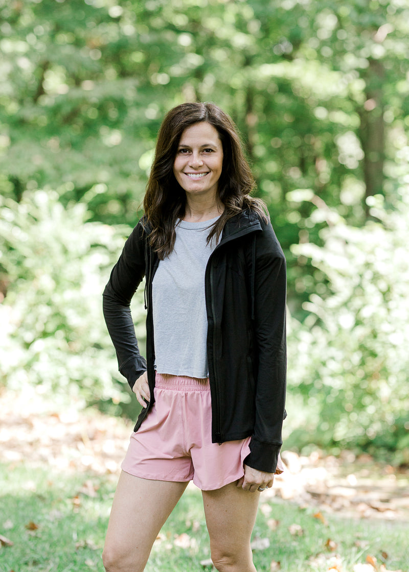 Brunette model wearing silver workout shirt, shorts and jacket.