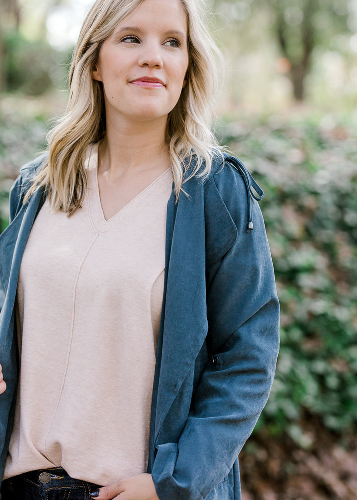 Blonde model wearing a slate blue jacket over a sand top.